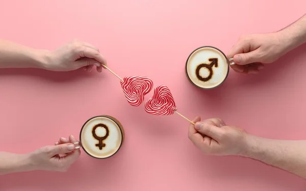 Fundo rosa com dois cafés com símbolos femininos e masculinos. No meio, dois pirulitos em formato de coração