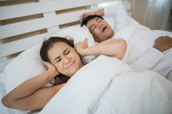 Mulher tampando os ouvidos para não ouvir o marido dormindo enquanto ele ronca e perdendo o desejo sexual