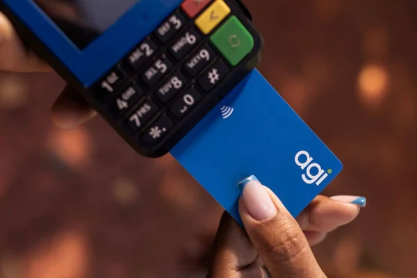 Imagem colorida mostra mão feminina inserindo cartão com logotipo Agibank em máquina de cartões - Metrópoles