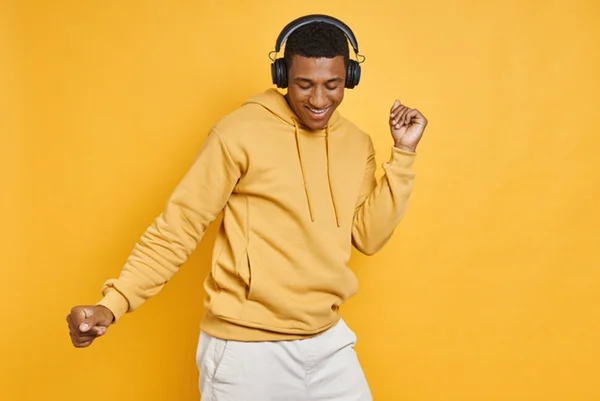 Foto de homem com casaco amarelo dançando com fone de ouvido - Metrópoles - música
