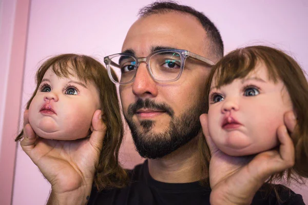Foto colorida mostra homem de óculos e barba, segurando a cabeça de duas bonecas - Metrópoles