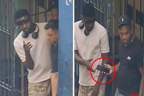 Homem entrega discretamente celular par a outro, em frente a portão de imóvel - Metrópoles