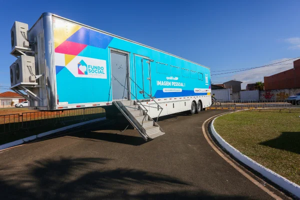 Imagem mostra uma carreta azul com o logotipo do Fundo Social, estacionada em área aberta, com estrutura adaptada para cursos profissionalizantes.