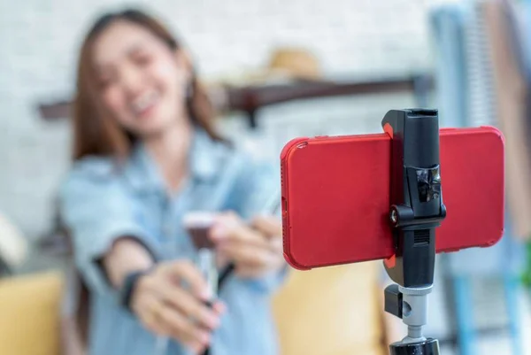 Na foto há um celular em cima de um suporte com uma mulher ao fundo gravando vídeo - Metrópoles