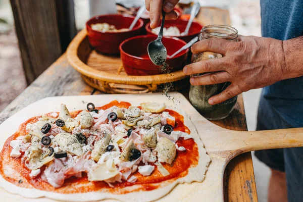 homens temperando uma pizza com orégano - Metrópoles