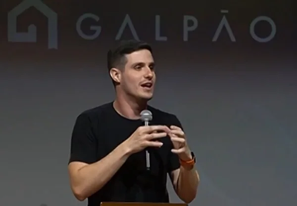 Em foto colorida homem branco de camiseta preta fala do microfone - Metrópoles