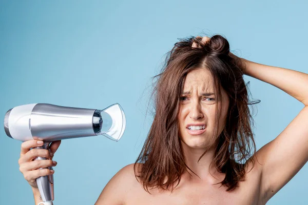Foto colorida de mulher pegando no cabelo e segurando um secador - Metrópoles