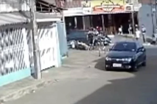 carro parado na rua e dois homens agredindo um terceiro que já está caído no chão