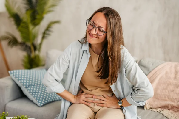 Foto colorida de mulher sentada em sofá e com as mãos na barriga - Metrópoles