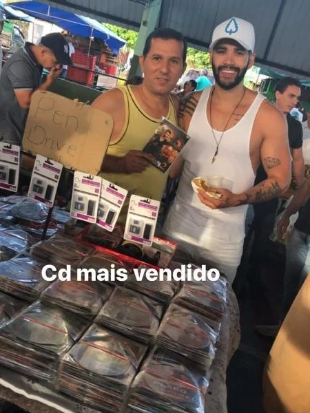 Gusttavo Lima aproveitou a parada em uma feira e tirou foto com o ambulante que vendia seu álbum pirateado Gusttavo Lima aproveitou a parada em uma feira e tirou foto com o ambulante que vendia seu álbum pirateado