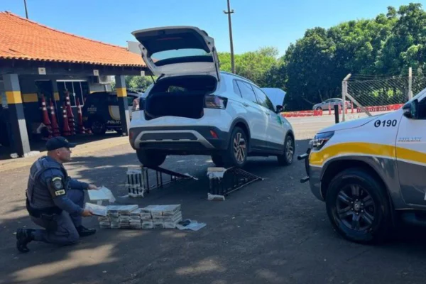 Imagem colorida mostra policial militar (PM) retirando pacotes de cocaína de parte de baixo de um carro que transportava a droga em um fundo falso - Metrópoles