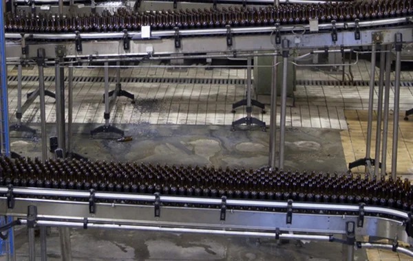 Imagem colorida de uma esteira de uma fábrica de bebidas com garrafas