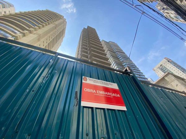 Imagem colorida mostra placa de obra embargada com prédio ao fundo - Metrópoles