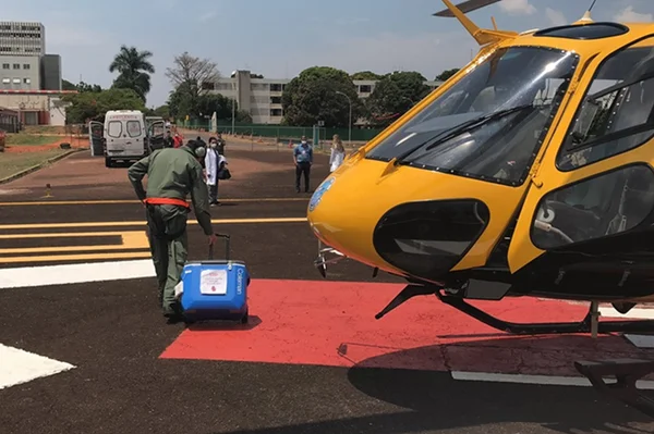 Helicóptero amarelo e preto no chão e pessoas andando com mala