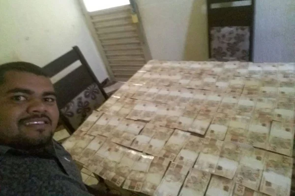 Foto colorida de homem perto a mesa cheia de notas de dinheiro