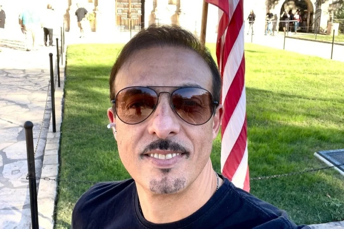 Imagem colorida de homem de óculos escuros sorrindo. Metrópoles