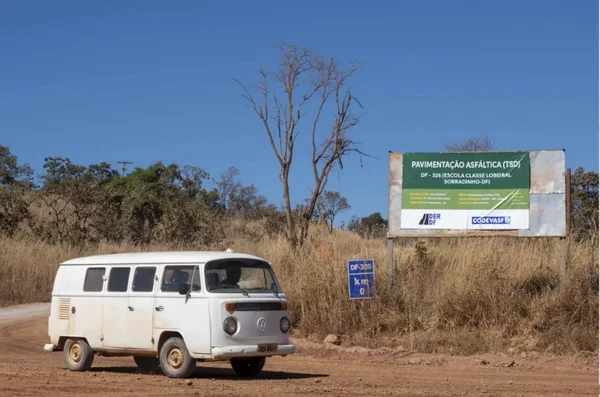 imagem de uma kombi branca andando em uma estrada sem asfalto com uma placa da codevasf ao fundo