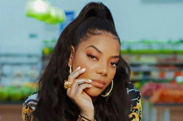 Cantora Ludmilla posando para foto. Ela usa roupa estampada, está com cabelos presos e olha seriamente para a câmera - Metrópoles