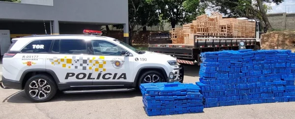 Imagem colorida mostra 991 tijolos de maconha apreendidos com caminhoneiro ao lado de um carro de polícia - Metrópoles