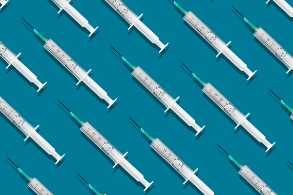 Seringas médicas organizadas em um padrão em fundo azul. Metrópoles vacina demência