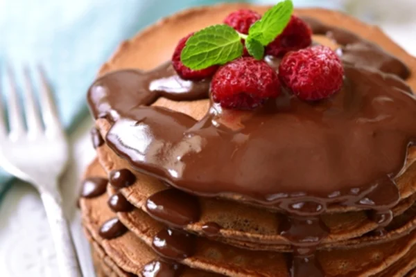 Panqueca de chocolate com calda de chocolate e frutas vermelhas por cima, decoradas com ramo de hortelã - Metrópoles