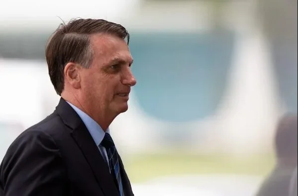 Bolsonaro aparece de perfil, usando terno e gravata, sem máscara, em algum lugar do Palácio da Alvorada, sorrindo - Metrópoles