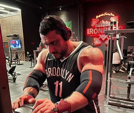 Imagem de homem em academia, com fone de ouvido e regata preta - Metrópoles