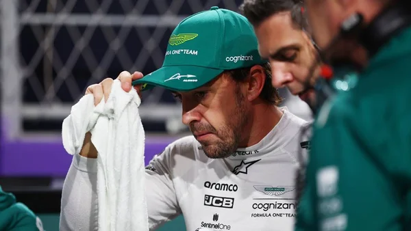 Foto do piloto Fernando Alonso com macacão branco, com semblante triste e colocando a mãe em seu boné que está na cabeça - Metrópoles