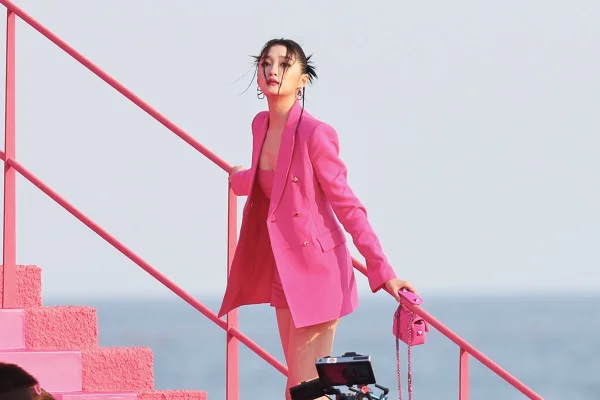 A atriz Guan Xiaotong, uma mulher asiática jovem e branca, de cabelo liso preto, posa para foto no desfile da marca Valentino. Ela usa um vestido, um blazer e uma bolsa, todo na cor rosa shocking. - Metrópoles