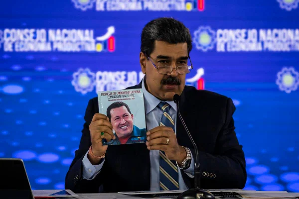 Imagem colorida mostra o presidente da Venezuela, Nicolás Maduro, segurando um livro com a foto do ex-presidente do país Hugo Chávez - Metrópoles