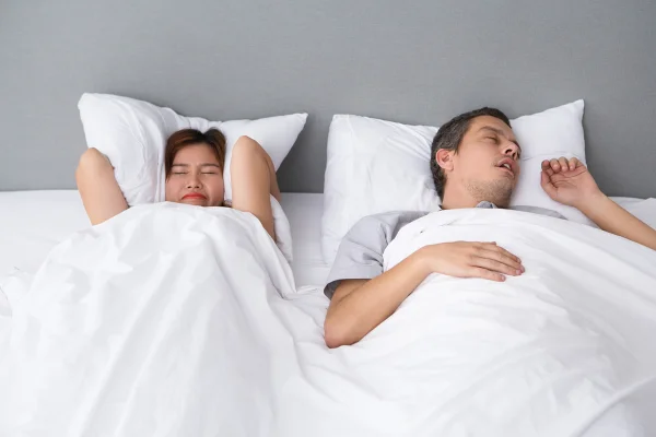 Mulher com braços na cabeça enquanto homem dorme roncando - Metrópoles