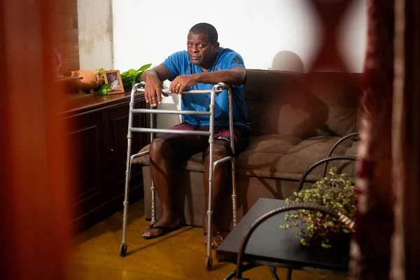 Foto colorida de homem segurando andador na porta de casa