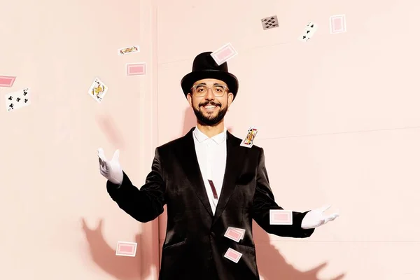Foto colorida de Raphael Montes vestido de mágico com cartas voando ao seu redor - Metrópoles