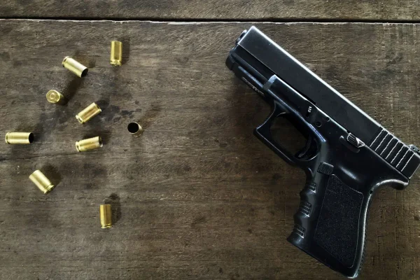 Foto colorida de balas vazias e uma arma em uma mesa
