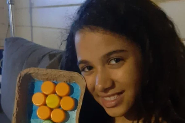 Imagem colorido de menina com o rosto ao lado de um pote com objetos redondos. Metrópoles