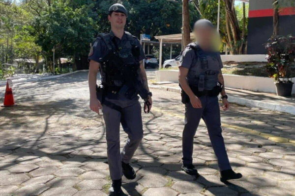 Dois PMs fardados, com boinas, caminham em área aberta, sob a luz do sol - Metrópoles