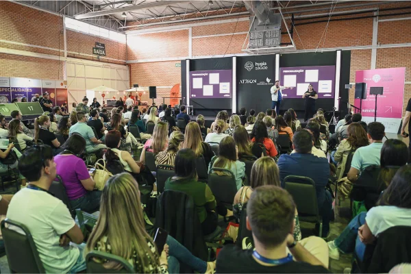 Foto colorida de um evento, na imagem várias pessoas sentadas assistindo uma palestra