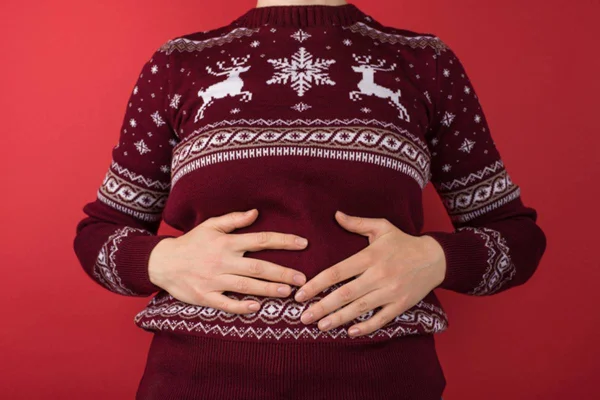 Imagem colorida de pessoa inchada com mão na barriga e roupa de Natal - Metrópoles