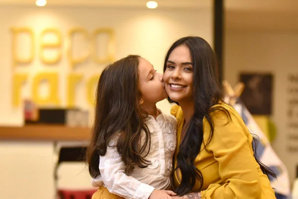 Criança branca beijando o rosto de mulher branca em uma loja de shopping