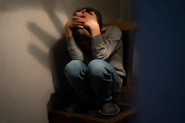 Menino em cima de uma cadeira encolhido. Conceito de violência infantil. Metrópoles