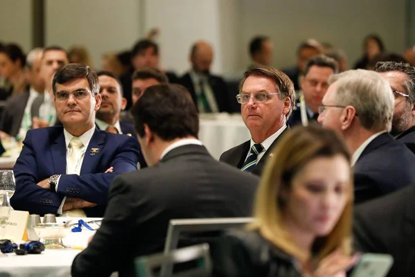 Bolsonaro sentado em mesa com outros homens em evento nos EUA