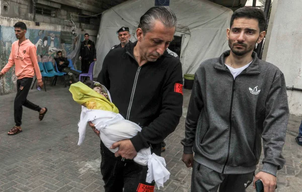 Homem carrega o cadáver de uma criança para enterro no necrotério do Hospital En-Neccar em Rafah, Gaza - metrópoles