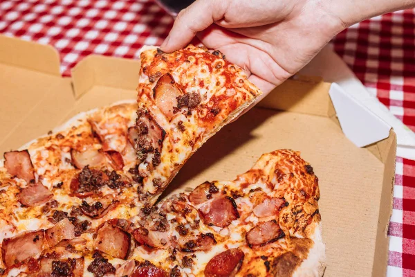 Foto colorida de uma mão pegando um pedaço de pizza - Metrópoles.