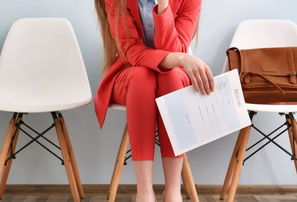 Mulher segurando curriculum na mão para vaga de emprego com terno vermelho sentada na cadeira - Metrópoles