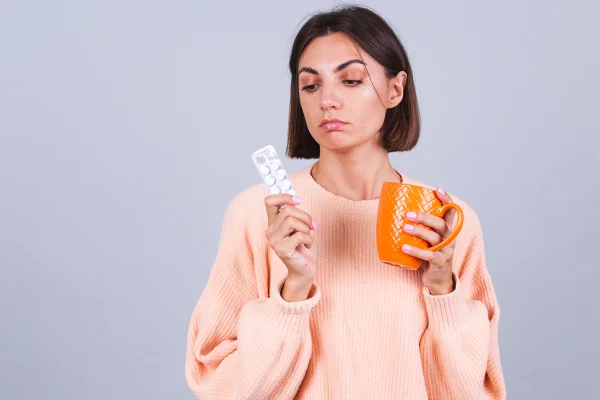Foto colorida de mulher segurando cartela de anticoncepcional e uma xícara de água de cor laranja - Metrópoles.
