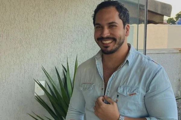 Imagem colorida mostra homem com uma camisa clara sorrido com a mão no peito; ele é um cotista que teve a matrícula rejeitada pela USP pela regra das cotas - Metrópoles