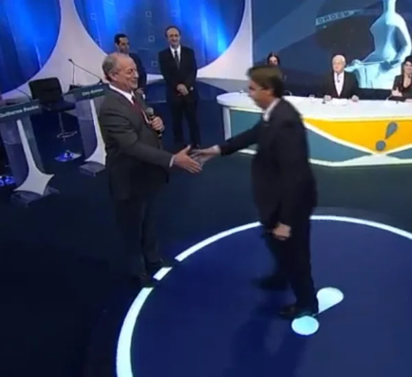 Em estúdio da RedeTV!, Ciro Gomes cumprimenta Bolsonaro, ambos candidatos nas eleições de 2018. Ao redor deles jornalistas observam - Metrópoles