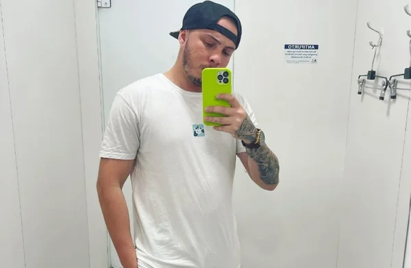 Imagem mostra homem de camisa branca, boné virado para trás, segurando celular - Metrópoles