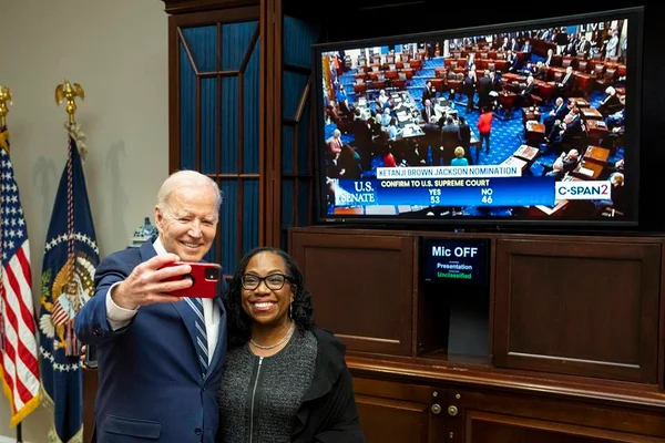 Presidente dos Estados Unidos, Joe Biden tira selfie com Ketanji Brown Jackson, a primeira mulher negra a integrar a Suprema Corte no país. Atrás, a televisão com sua aprovação no Senado - Metrópoles