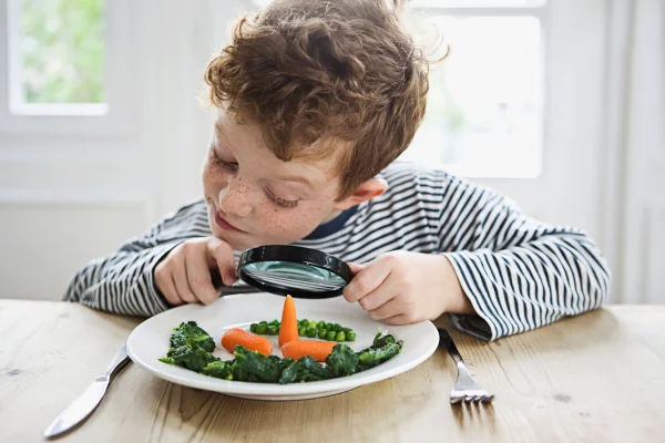 Foto mostra Menino (7-9 anos) olhando por cima de uma lupa durante o jantar.Criança comendo vegetais dieta vegetariana, vegana